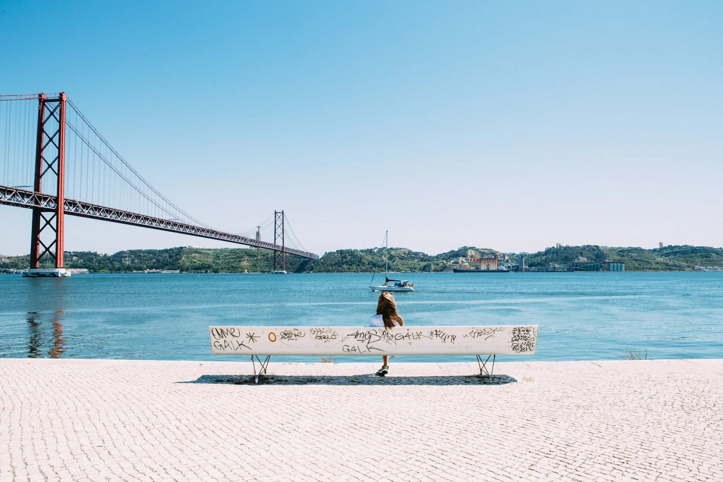 A woman sitting alone on a bench by the Lisbon waterfront